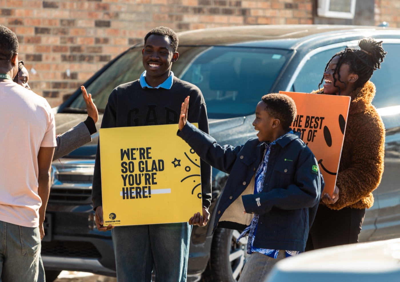 A boy high-fiving a greeter holding a sign that reads 'We're so glad you're here!'