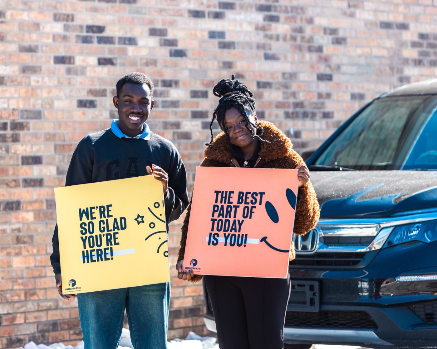 Greeters outside the church holding signs that read 'We're so glad you're here!' and 'The best part of today is you!'